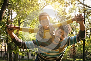 Smiling African American father carrying his daughter on piggyback and holding hands.