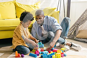 smiling african american father and little son playing with colorful blocks together