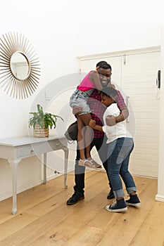 Smiling african american father returning home embracing son and daughter in hallway