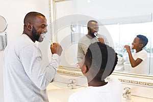 Smiling african american father and son having fun brushing teeth together in bathroom