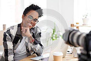 Smiling black millennial woman shooting at workplace