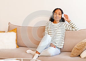 Smiling African-American female listening to music in headphones while sitting on couch
