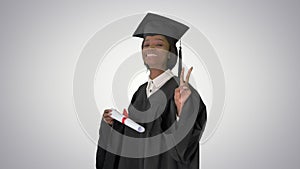 Smiling African American female student in graduation robe posing with diploma on gradient background.