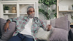 Smiling African American guy is using smartphone to make online video call talking and laughing looking at screen