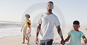 Smiling african american holding hands and walking on sunny beach