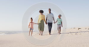 Smiling african american holding hands and walking on sunny beach