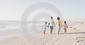 Smiling african american holding hands and walking on sunny beach