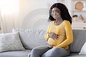Smiling african american lady carrying baby, hugging her big tummy