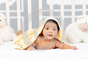 Smiling African-American little baby lies in bed after a bath in a yellow towel