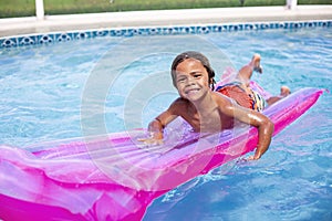 Smiling African American little boy playing in the swimming pool with an inflatable raft.