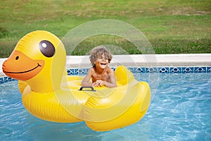 Smiling African American little boy playing in the swimming pool with a large inflatable duck.