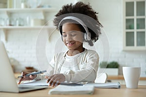 Smiling African American little girl wearing headphones studying at home