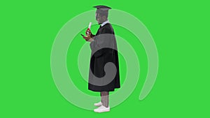 Smiling african american male student in graduation robe with diploma texting on the phone on a Green Screen, Chroma Key