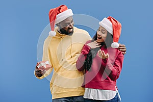 smiling african american man in christmas hat gifting present box to girlfriend