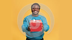 Smiling African American man holding gift box in hands, looking at camera and stretching present