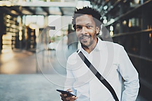 Smiling African American man holding mobile phone in hands and looking to the camera.Blurred background.