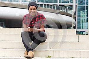 Smiling african american man listening to music with mobile phone and earphones outside in the city