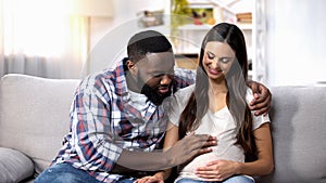Smiling African-American man stroking his pregnant wife tummy, future parents