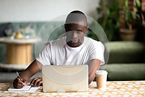 Smiling African American man using laptop, making notes