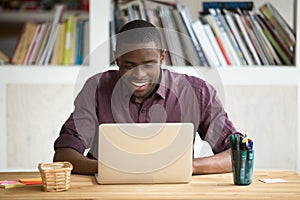 Smiling african-american man using laptop sitting at home office