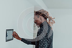 Smiling African American man using modern smart home system, controller on wall, positive young man switching