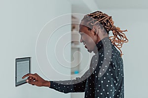 Smiling African American man using modern smart home system, controller on wall, positive young man switching