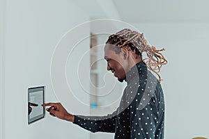 Smiling African American man using modern smart home system, controller on wall, positive young man switching