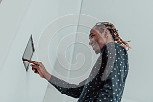 Smiling African American man using modern smart home system, controller on wall, positive young man switching