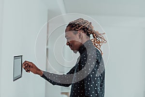 Smiling African American man using modern smart home system, controller on wall, positive young man switching