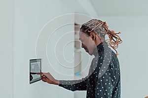 Smiling African American man using modern smart home system, controller on wall, positive young man switching