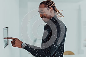 Smiling African American man using modern smart home system, controller on wall, positive young man switching