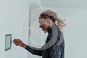 Smiling African American man using modern smart home system, controller on wall, positive young man switching