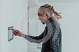 Smiling African American man using modern smart home system, controller on wall, positive young man switching