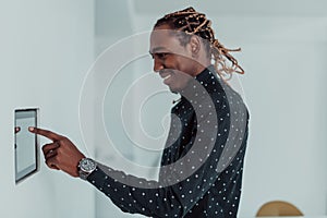 Smiling African American man using modern smart home system, controller on wall, positive young man switching