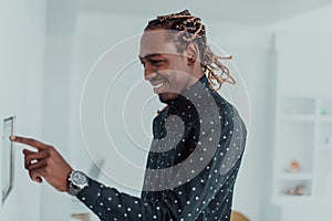 Smiling African American man using modern smart home system, controller on wall, positive young man switching