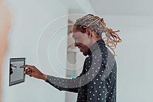 Smiling African American man using modern smart home system, controller on wall, positive young man switching