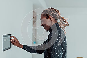 Smiling African American man using modern smart home system, controller on wall, positive young man switching