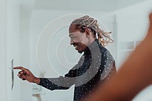 Smiling African American man using modern smart home system, controller on wall, positive young man switching