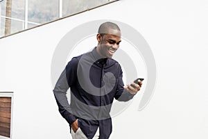 Smiling African American man walking with cellphone by white wall