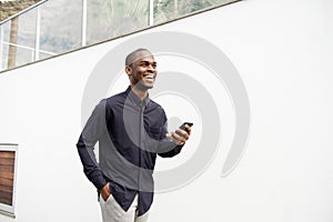 Smiling African American man walking with phone by white wall