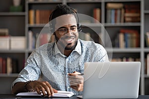 Smiling African American man wearing headphones looking at laptop screen