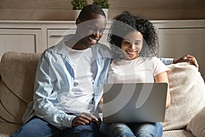 Smiling african american married spouse sitting at home with laptop.
