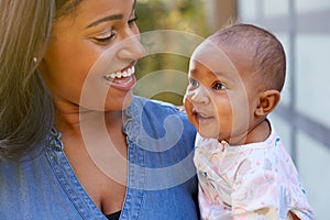 Smiling African American Mother Cuddling And Playing With Baby Daughter In Garden At Home