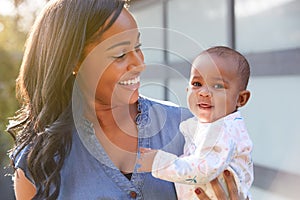 Smiling African American Mother Cuddling And Playing With Baby Daughter In Garden At Home