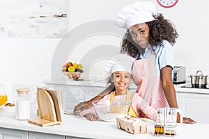 smiling african american mother and daughter in chef hats preparing dough