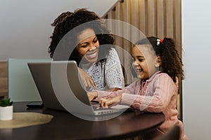 Smiling african american mother and daughter using laptop at home