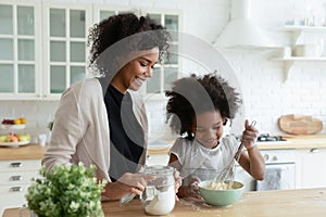 Smiling African American mother with little daughter cooking pancakes