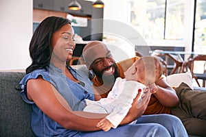 Smiling African American Parents Cuddling And Playing With Baby Daughter Indoors On Sofa At Home