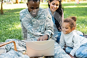 smiling african american soldier in military uniform using laptop with family