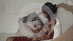 Smiling African American student woman using computer laying on the couch